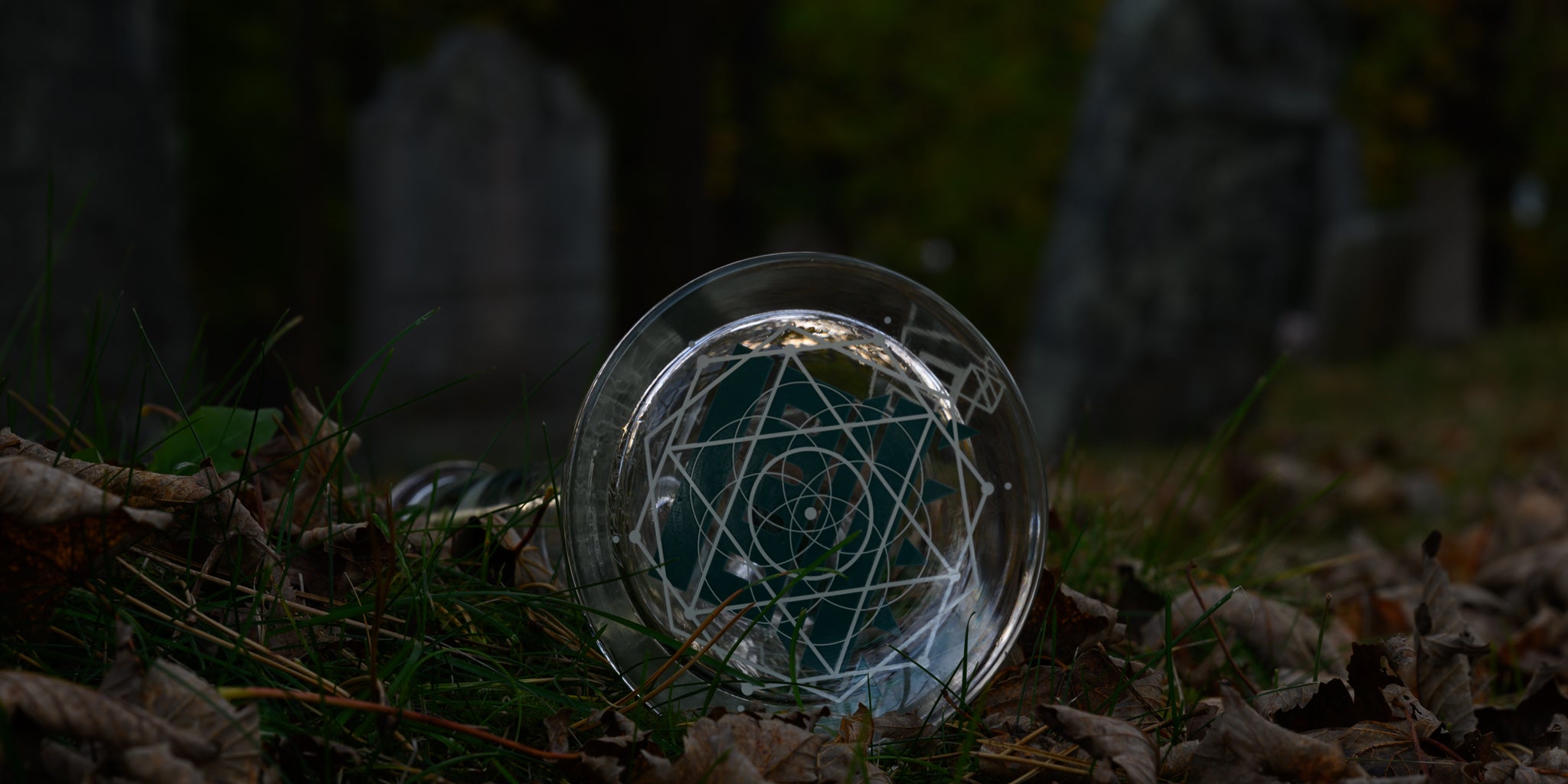 A glass bong with an intricate geometric etching rests on the ground among fallen leaves and overgrown grass in a dimly lit graveyard. The base features a mesmerizing, celestial-inspired design, its white lines contrasting sharply against the dark, moody background of weathered tombstones. The transparency of the glass reflects the faint light, adding an eerie glow to the scene. The composition evokes a haunting yet elegant aesthetic, blending high-end craftsmanship with a gothic, atmospheric setting.