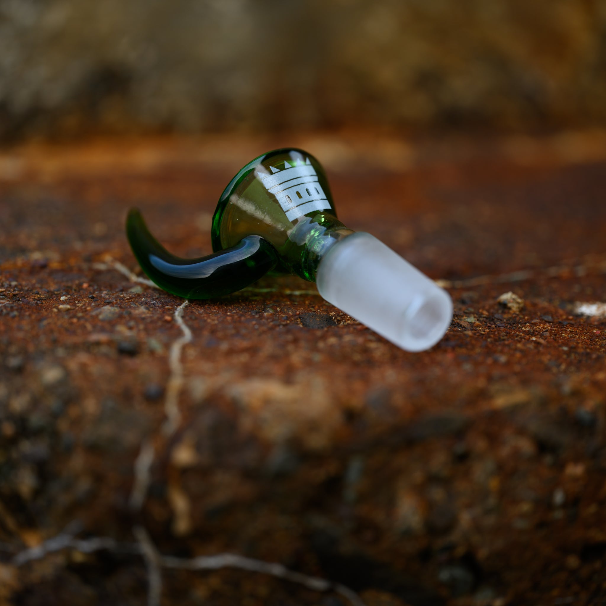 Close-up of a translucent green glass bowl attachment with a castle silhouette etched on it, resting on a rust-colored rock.