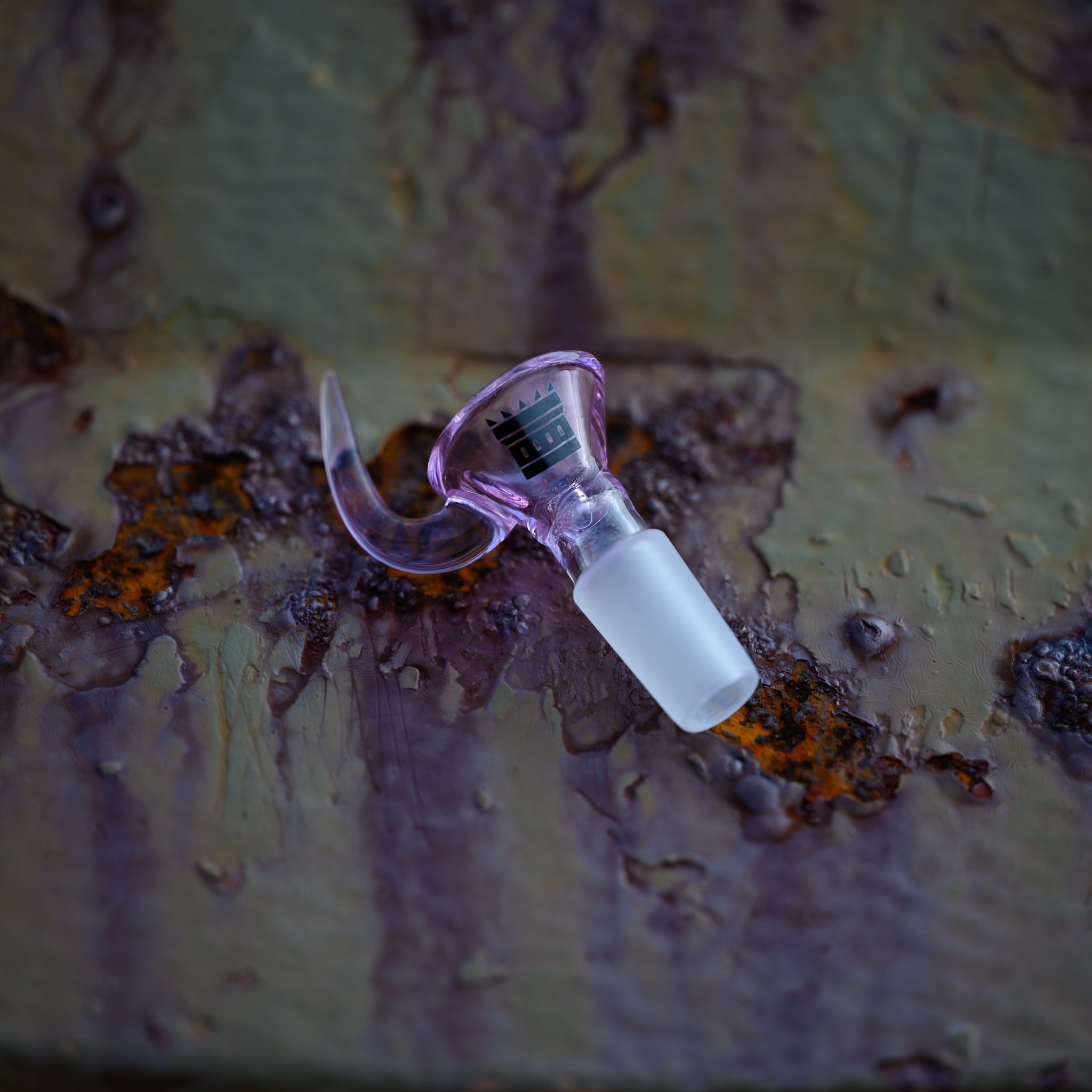 A pink, Castle-branded glass bowl with a frosted male joint and curved handle, resting on a rusted, patina-covered metal surface.
