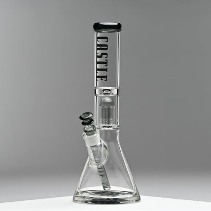 A glass beaker bong with the "Castle" logo prominently displayed on the neck, featuring an 8-arm percolator inside. The bong is set against a minimalist grey background, emphasizing its clean lines and modern design. The photo captures the bong from the left side, highlighting its structure and details.