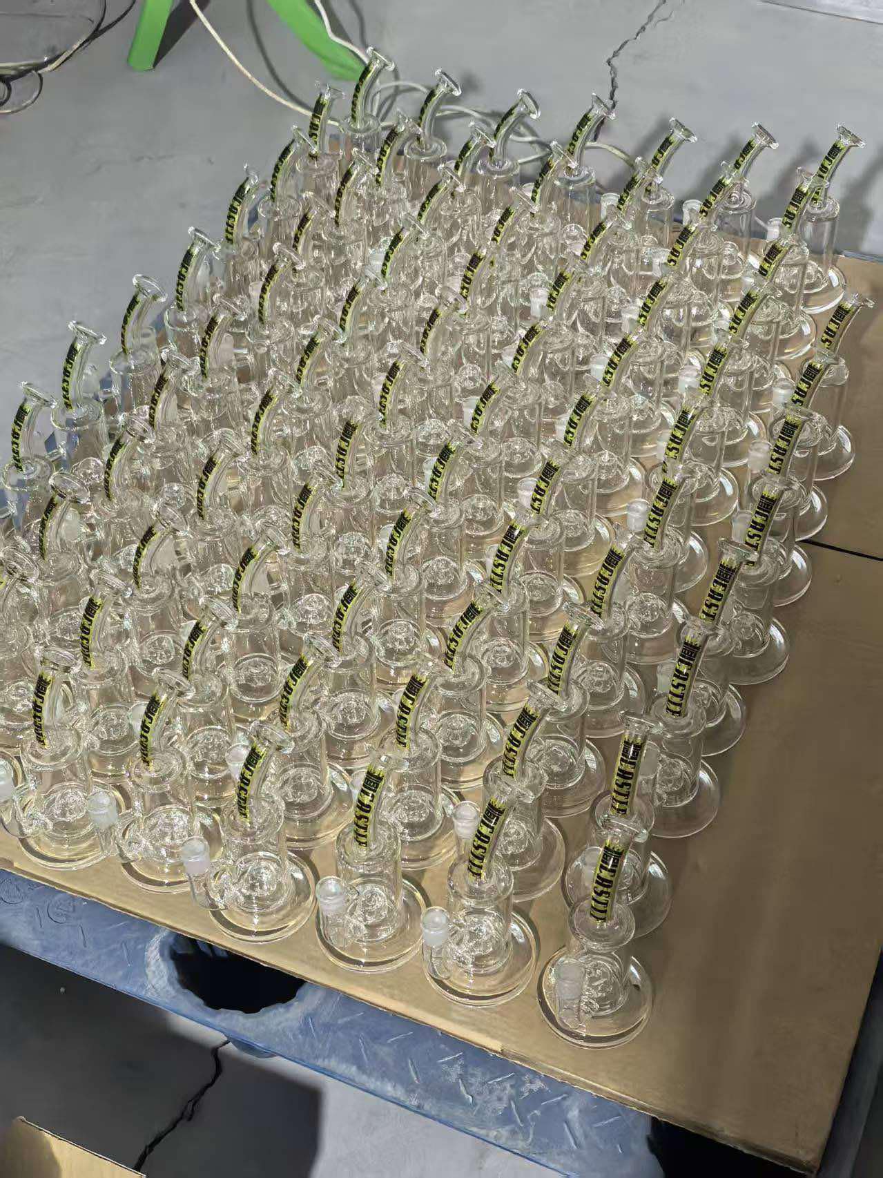 Dozens of identical clear glass dab rigs lined up in rows, each with the Castle Glassworks logo on the neck, arranged on cardboard.