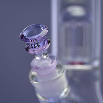 Close-up of the bowl of a glass bong with purple accents and the Castle Glassworks logo on the bowl. The background is a solid purple, highlighting the intricate design and craftsmanship of the bong. The image emphasizes the elegant detailing and quality of the glass, with the percolator visible in the background.
