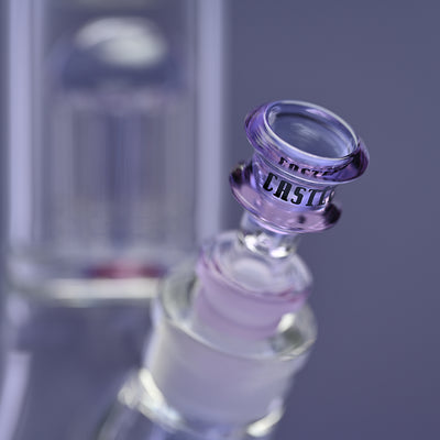 Close-up of the bowl of a glass bong with purple accents and the Castle Glassworks logo on the bowl. The background is a solid purple, highlighting the intricate design and craftsmanship of the bong. The image emphasizes the elegant detailing and quality of the glass, with the percolator visible in the background.