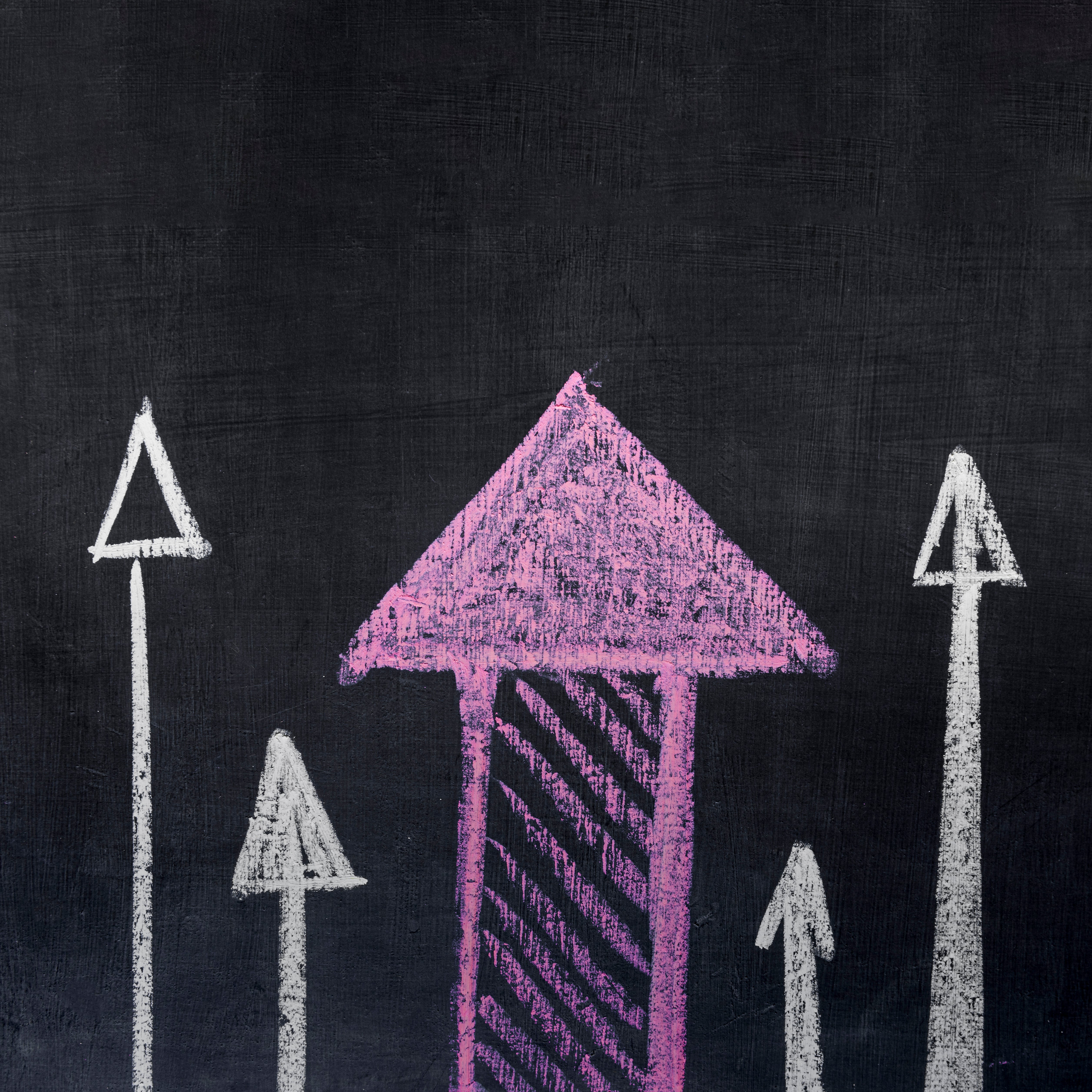 Chalkboard background with multiple upward-pointing arrows drawn in chalk, the largest arrow in pink and smaller arrows in white on either side.